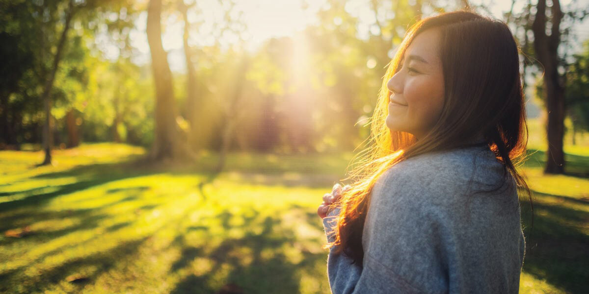 woman standing outside with trees grass and sunshine