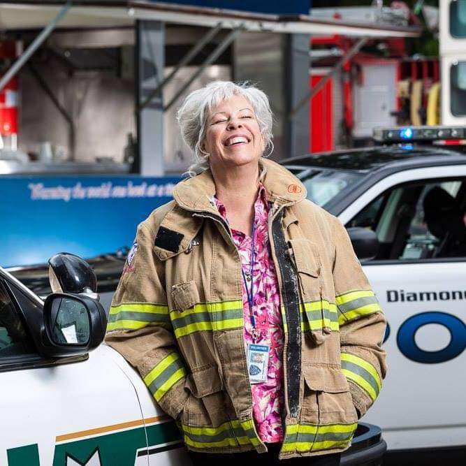 Mama Ginger laughing, wearing incident jacket, with patrol cars
