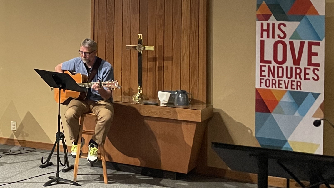 Pastor Steve Johnson Leading Worship with sign "His love endures forever" behind him