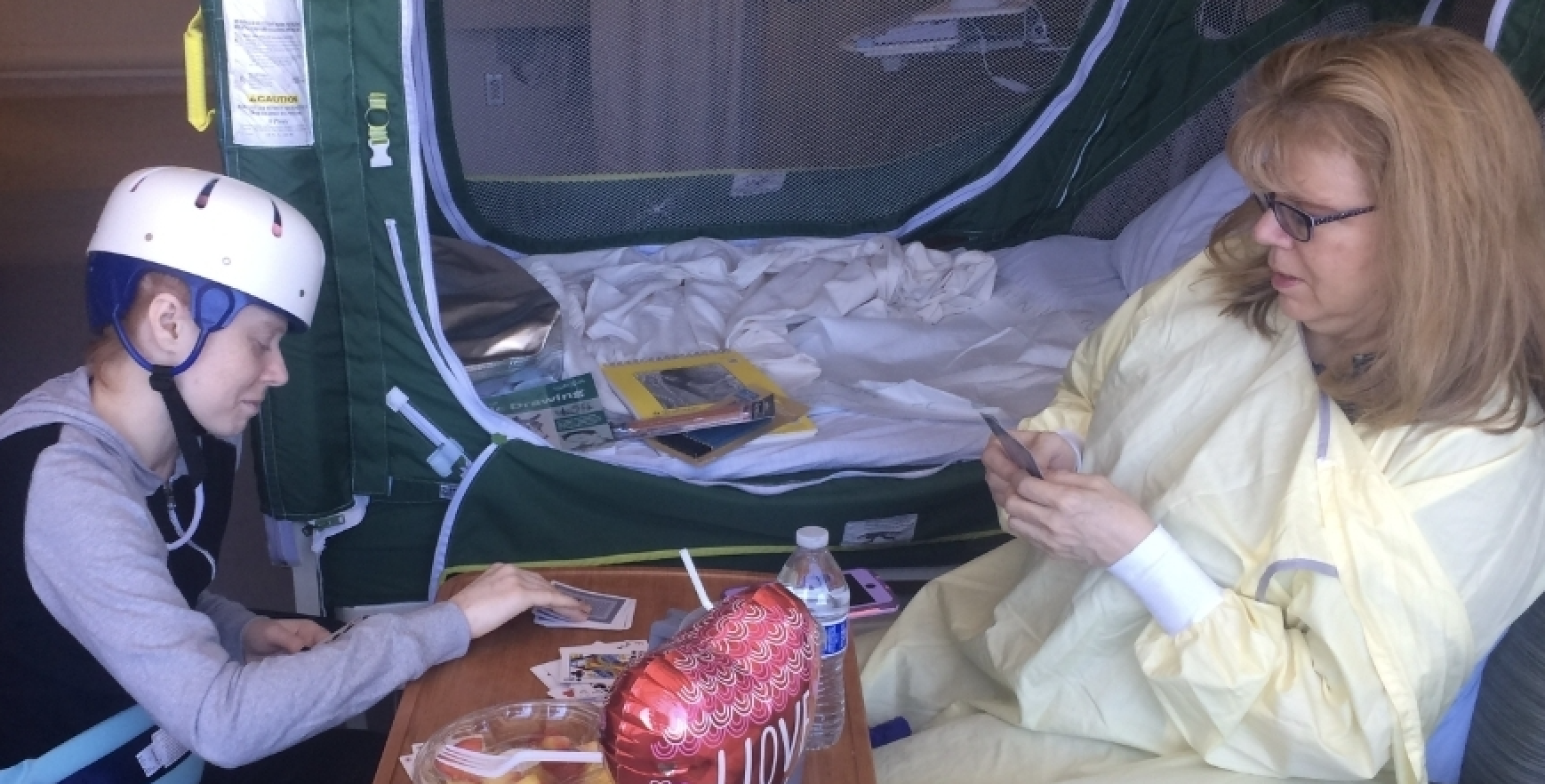 Woman with helmet with her mother, playing cards in the hospital