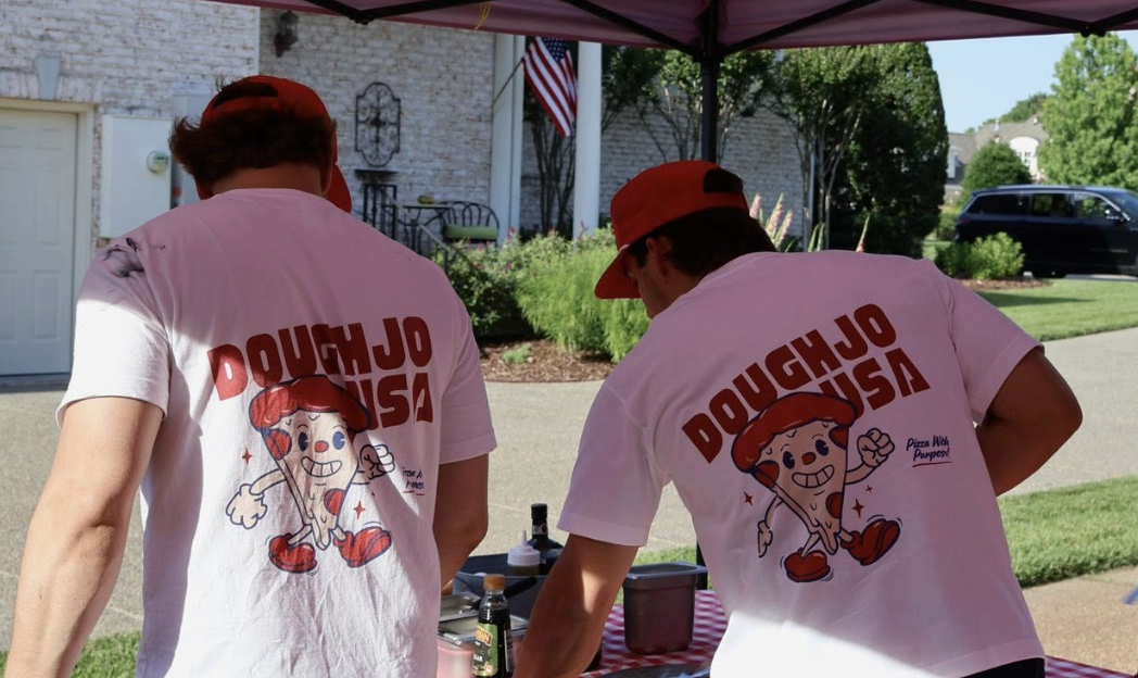 Two men under a tent with DoughJo USA T-shirts
