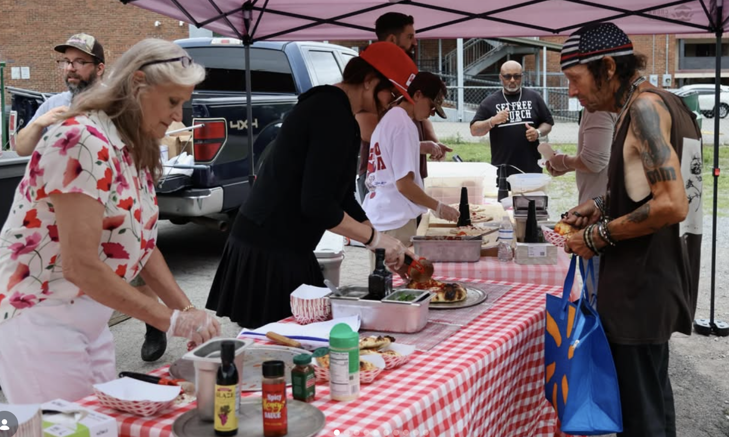 Woman and two men serve pizza to man with tattoos