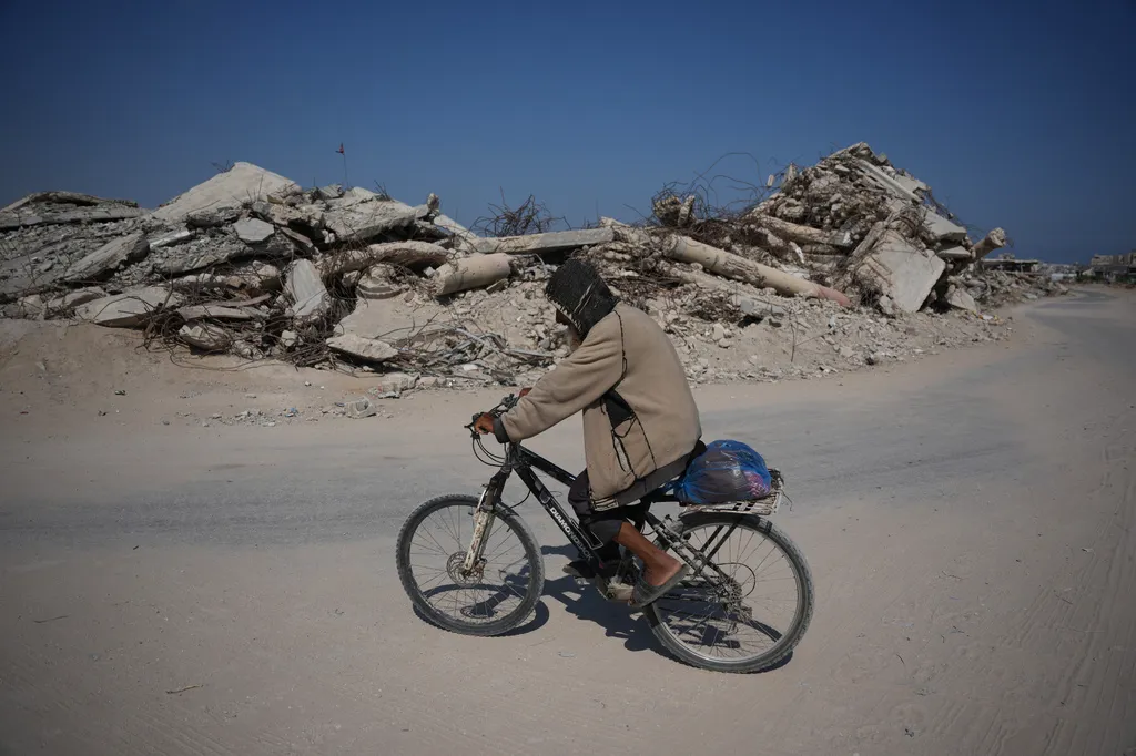 A Palestinian man rides his bicycle by the rubble of buildings that were destroyed during the Israel Hamas war