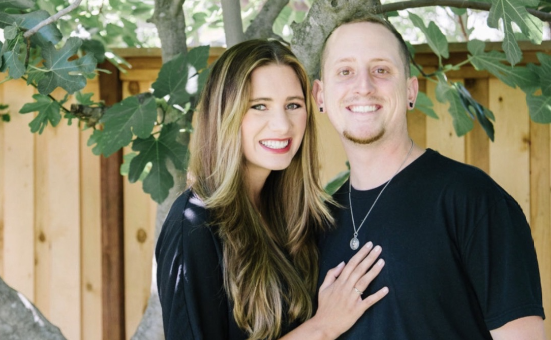 Smiling couple under a tree, outdoors with a fence in the background