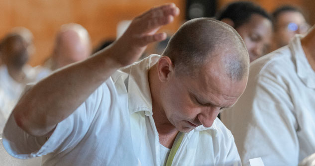 Man bowing head with hand raised wearing white prison garb
