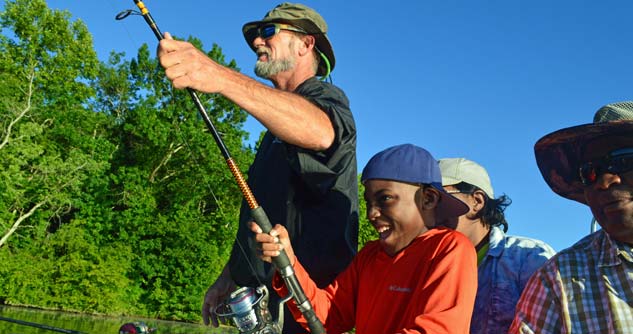 Excited boy holds fishing pole, assisted by CAD guide while family looks on