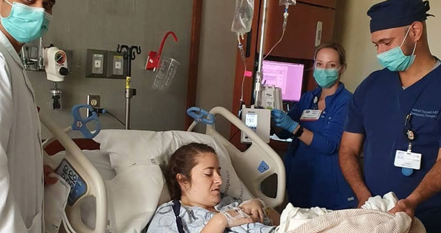 Woman lying in hospital bed, surrounded by doctors