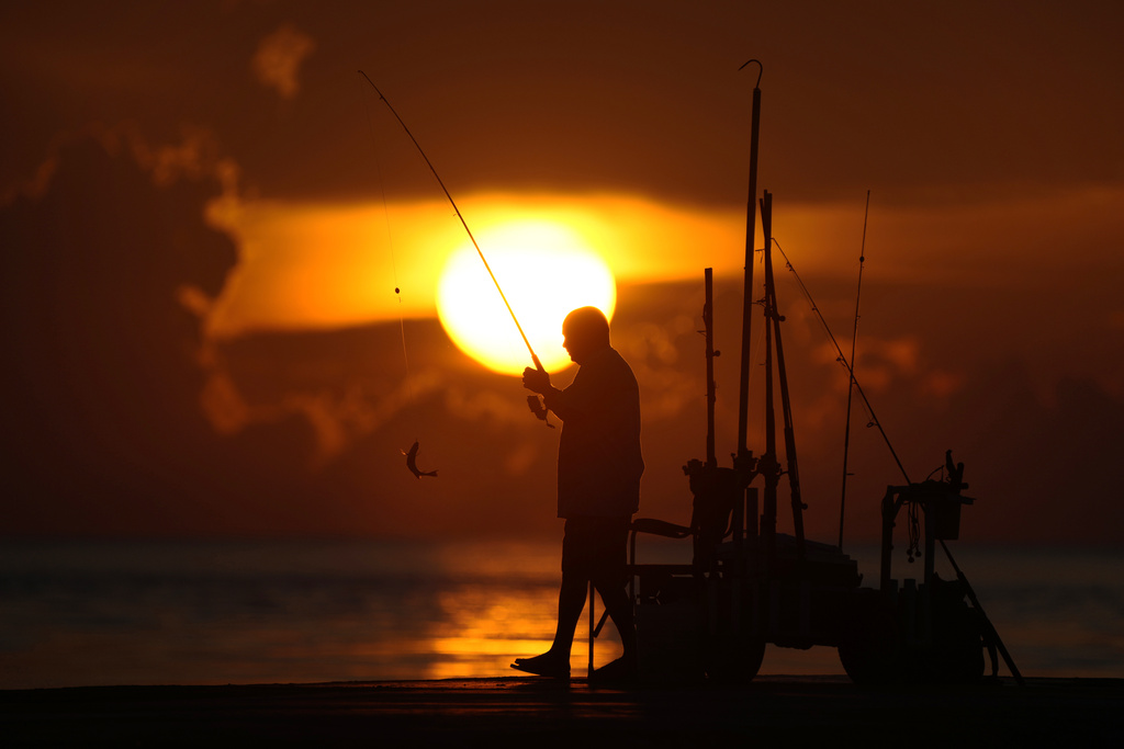 A fisherman reels in his catch as the sun rises over the Atlantic Ocean in Bal Harbour, Fla.