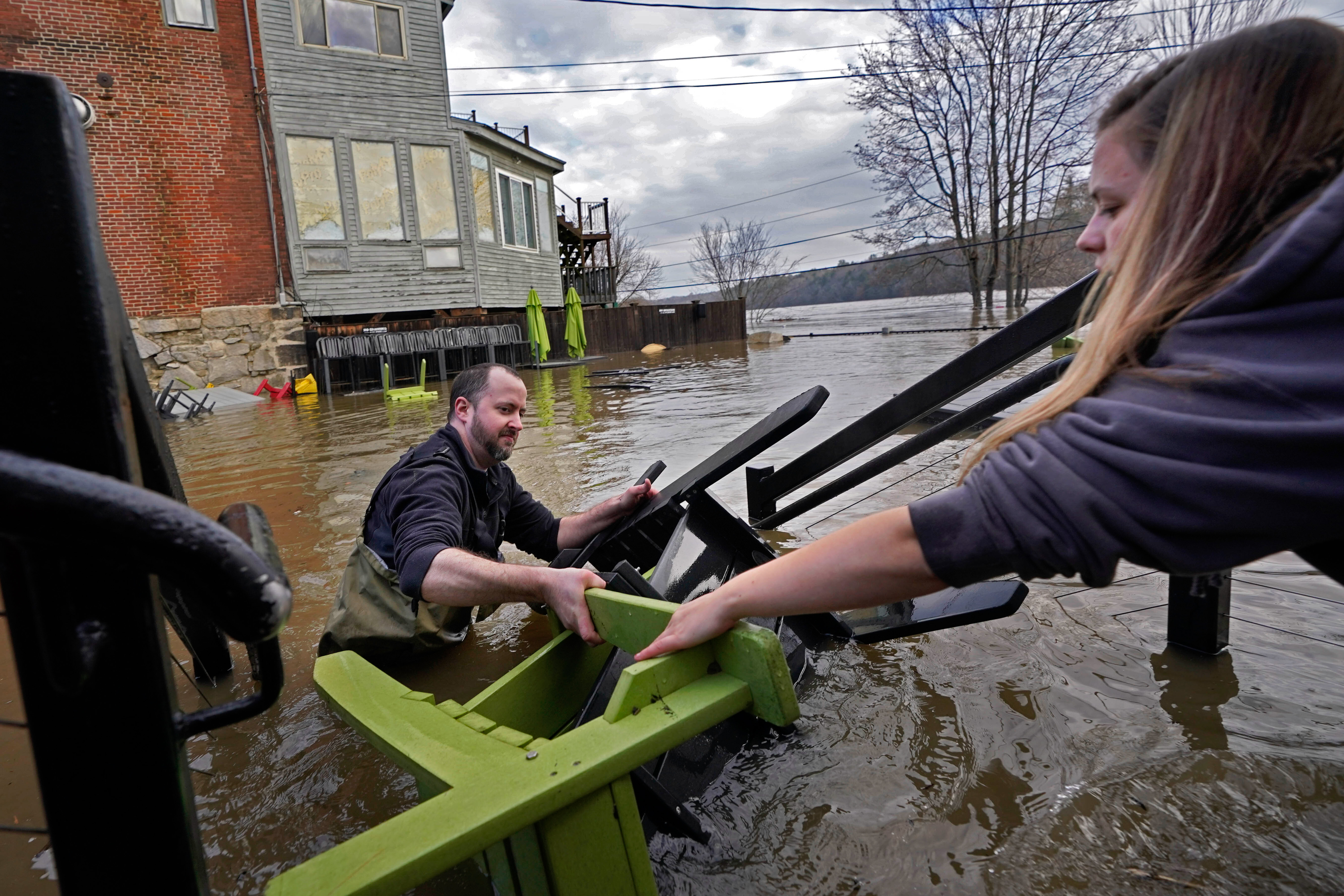 Man hands patio furniture to woman while he stands in floodwaters