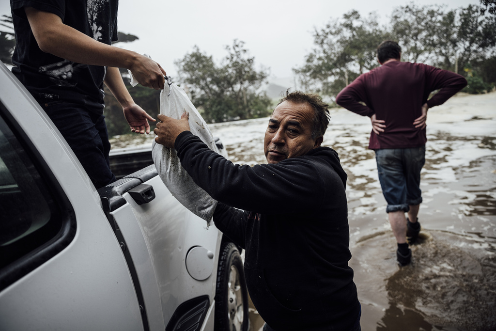 Man carries a sandbag to reinforce a home along a flooded Clarendon road due to high waves in Pacifica, California