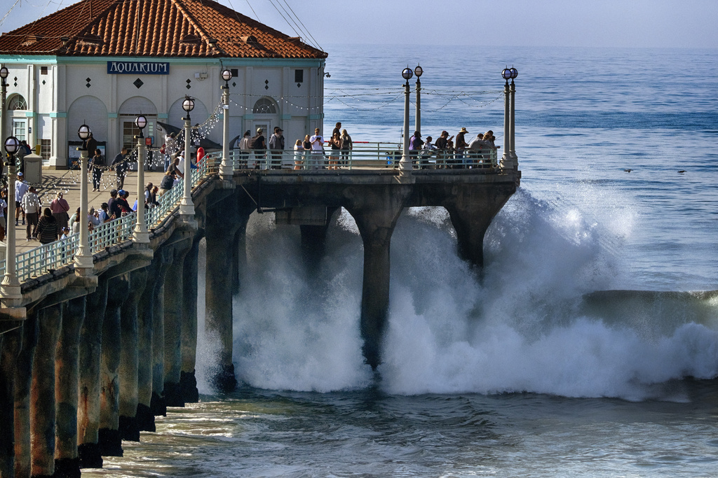 People watch as turbulent surf pounds the side of the pier in Manhattan Beach, Calif.