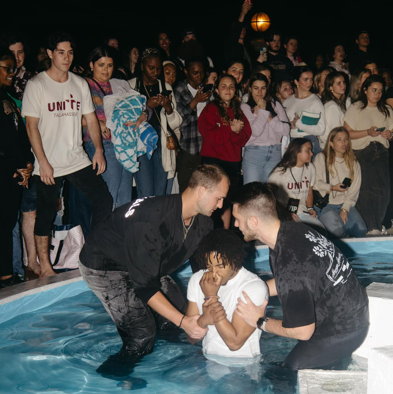 Two men dunking a young man in fountain while students watch