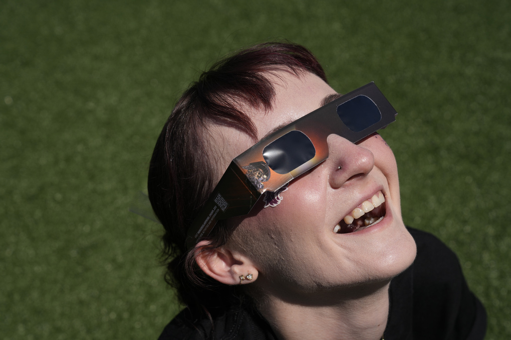 Jordan Elliott smiles as she watches with solar glasses as the moon starts to cross in front of the sun during a total solar eclipse in Carbondale, Ill.