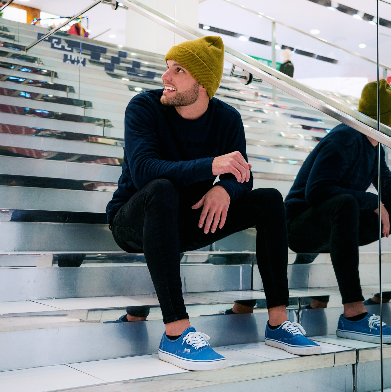 man sitting on stairs with black clothes, blue shoes and a brown hat